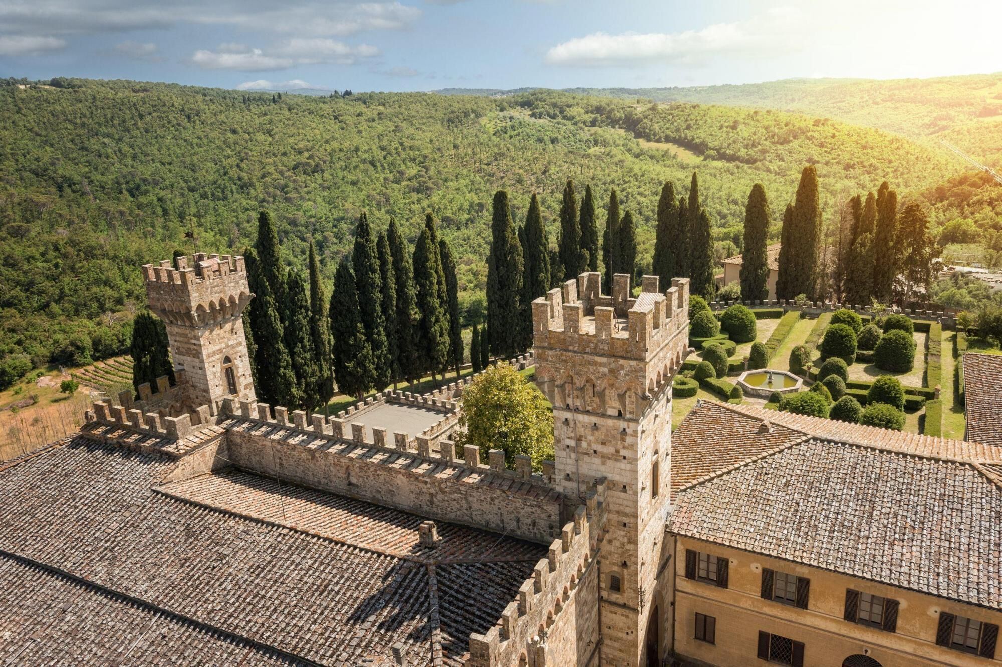 A historic castle with two prominent towers, surrounded by lush greenery and terraced gardens.