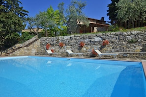 A swimming pool with lounge chairs and a stone wall with flowers. - La Badia 1 in Tavarnelle Val di Pesa (Barberino Tavarnelle)