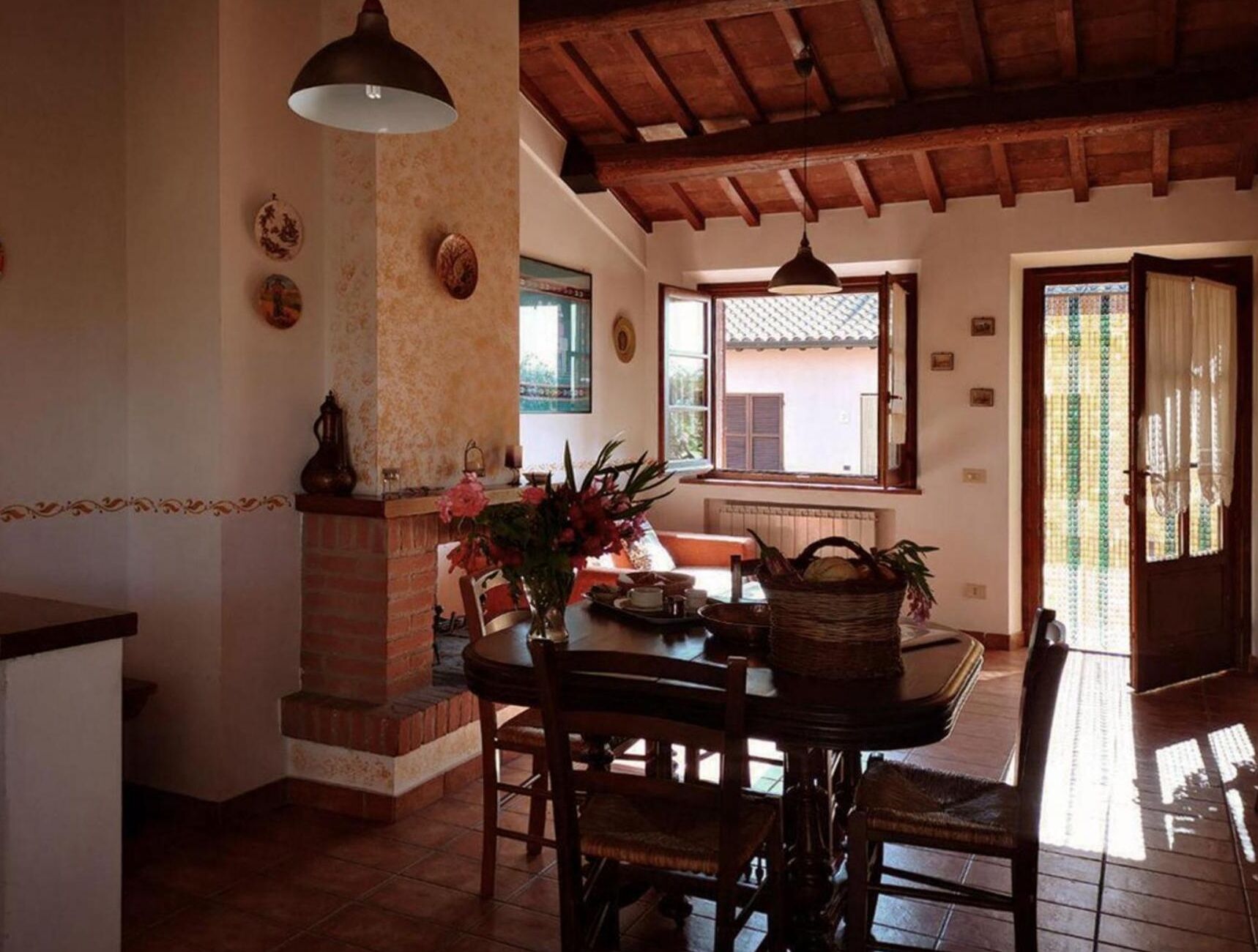 A dining area with a brick fireplace, a table set for two, and a window with a view of the outside.