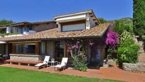 A modern house with a tiled roof, a stone facade, and a well-maintained garden with a lawn and flowering plants. - Villa Ada in Ansedonia (Orbetello)