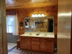 A wooden-paneled bathroom with a large mirror, two sinks, and a bench.