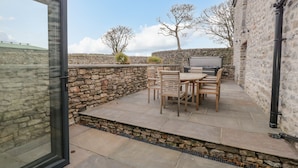 An outdoor patio with stone walls, a wooden table and chairs, and a TV screen. - Old Stable (Ulverston)