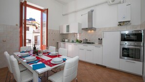 Une cuisine moderne avec des armoires blanches, un four encastré et un coin repas avec une table dressée pour quatre personnes.