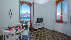 Une pièce comprenant une table à manger, des chaises, un téléviseur posé sur un meuble blanc et un sol à motifs.