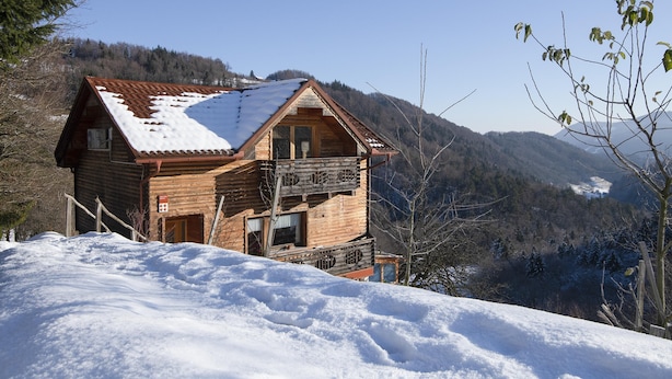 A wooden cabin with a sloped roof, surrounded by snow-covered hills and trees. - Pool Wellness Chalet Sunshine (Vransko)