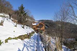 Une cabane en bois, dotée d’un toit en pente, entourée de collines et d’arbres couverts de neige.