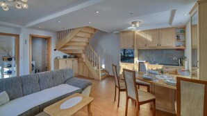 A modern kitchen with wooden cabinets, a dining area with a wooden table and chairs, and a staircase leading to an upper level. - Pool Wellness Chalet Sunshine (Vransko)