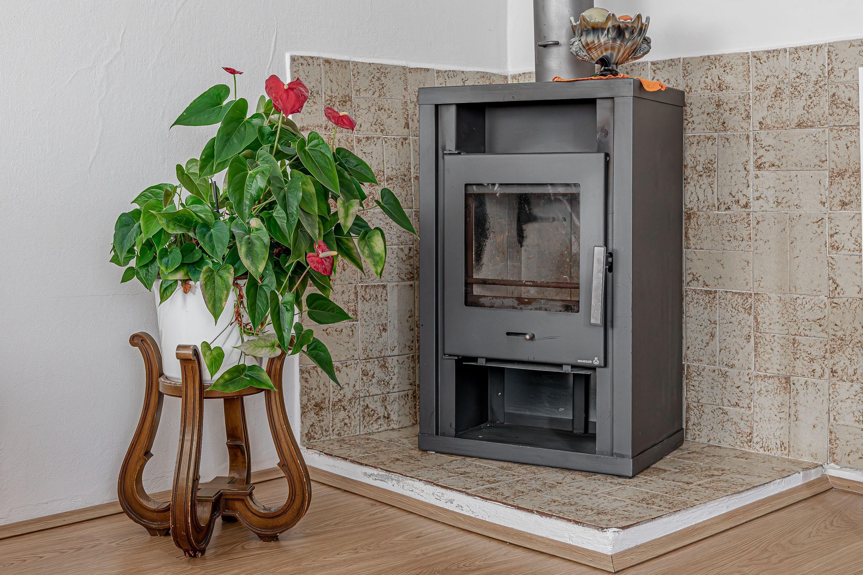 A corner room with a built-in wood stove, a potted plant, and a wooden stool.