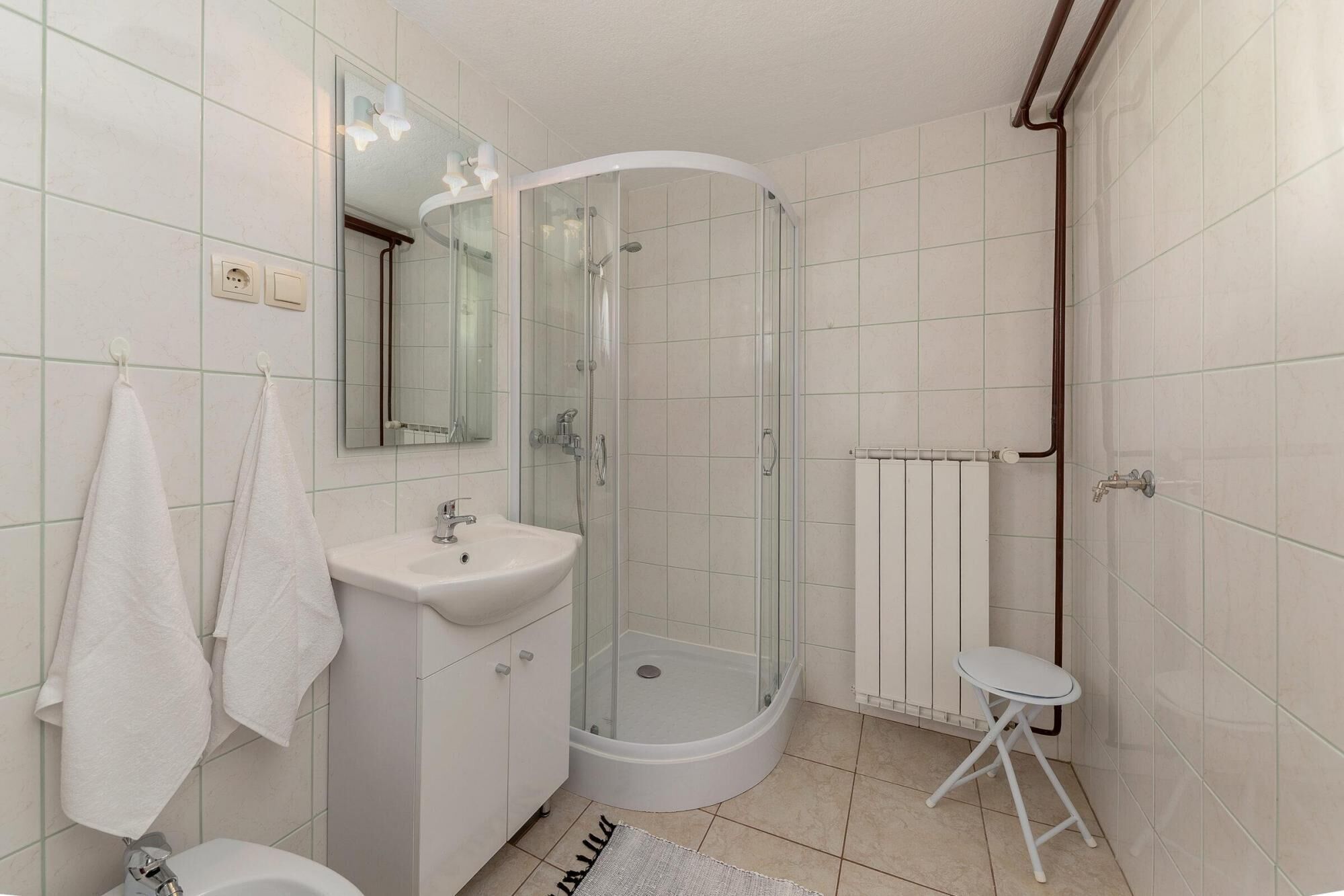 A modern bathroom with a glass-enclosed shower, a white sink, and a small white stool.