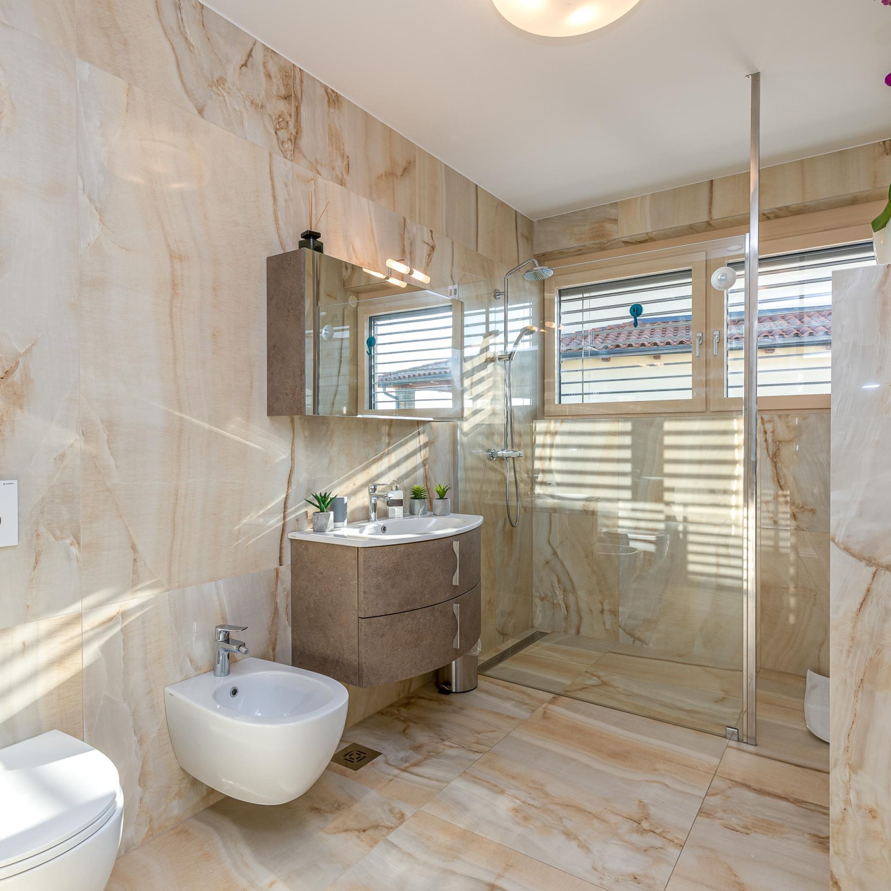 A modern bathroom with a marble floor, a bidet, a vanity with a mirror, and a glass-enclosed shower.