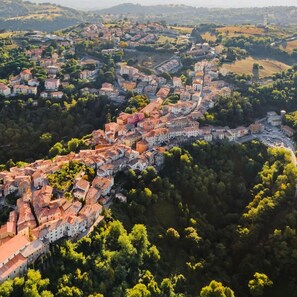 An aerial view of a town with a winding road through a valley, surrounded by greenery and buildings with red-tiled roofs. - Villa Borgiano in Scansano (Scansano)