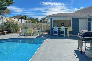 Un patio trasero con piscina, mobiliario exterior y una parrilla.