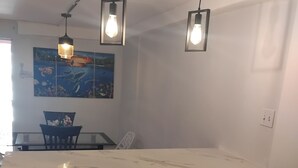 Cocina con encimera de mármol, estufa a gas, luces colgantes y un cuadro en la pared.