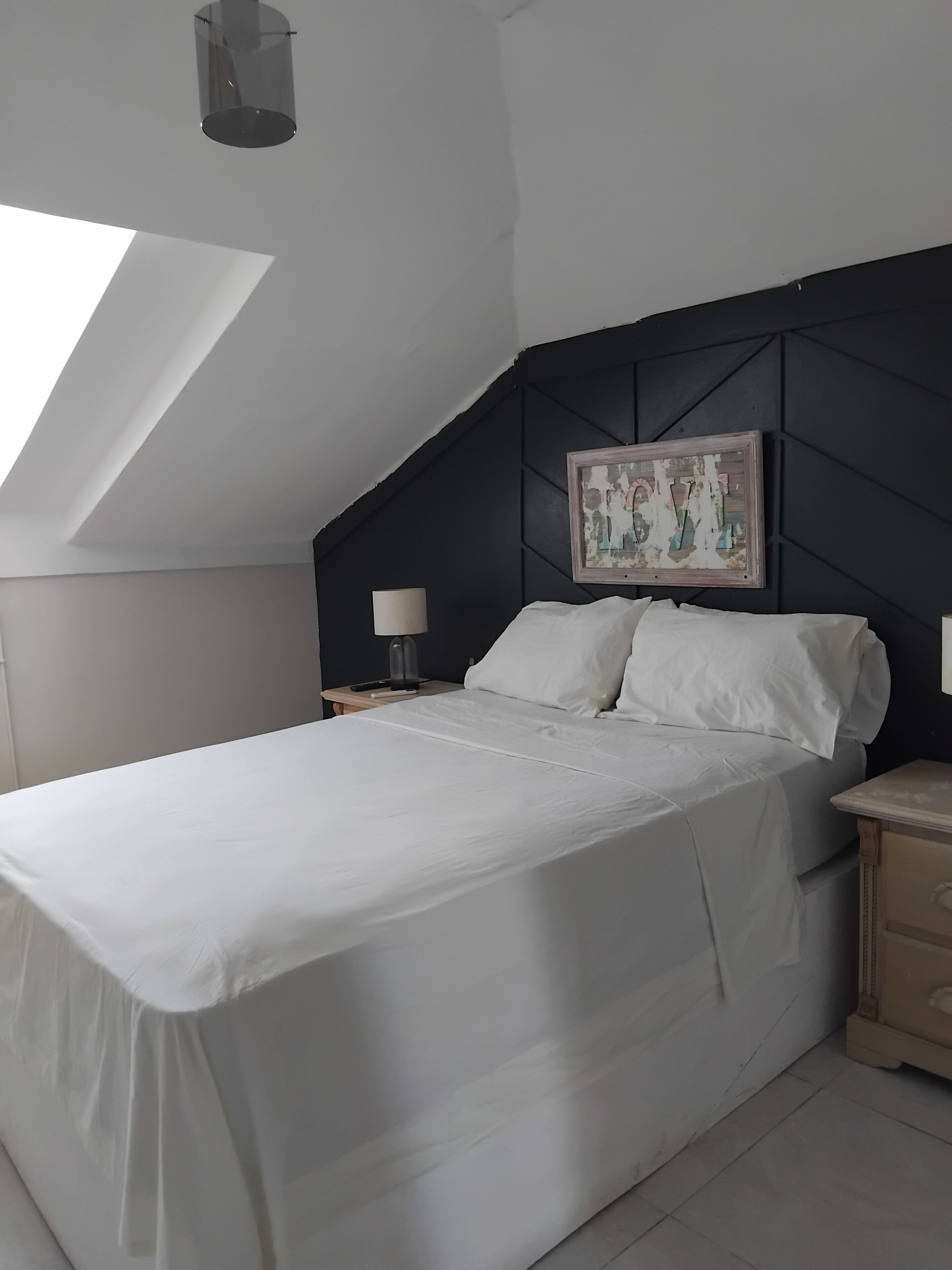 A bedroom with a bed, a nightstand, a lamp, and a painting on the wall.