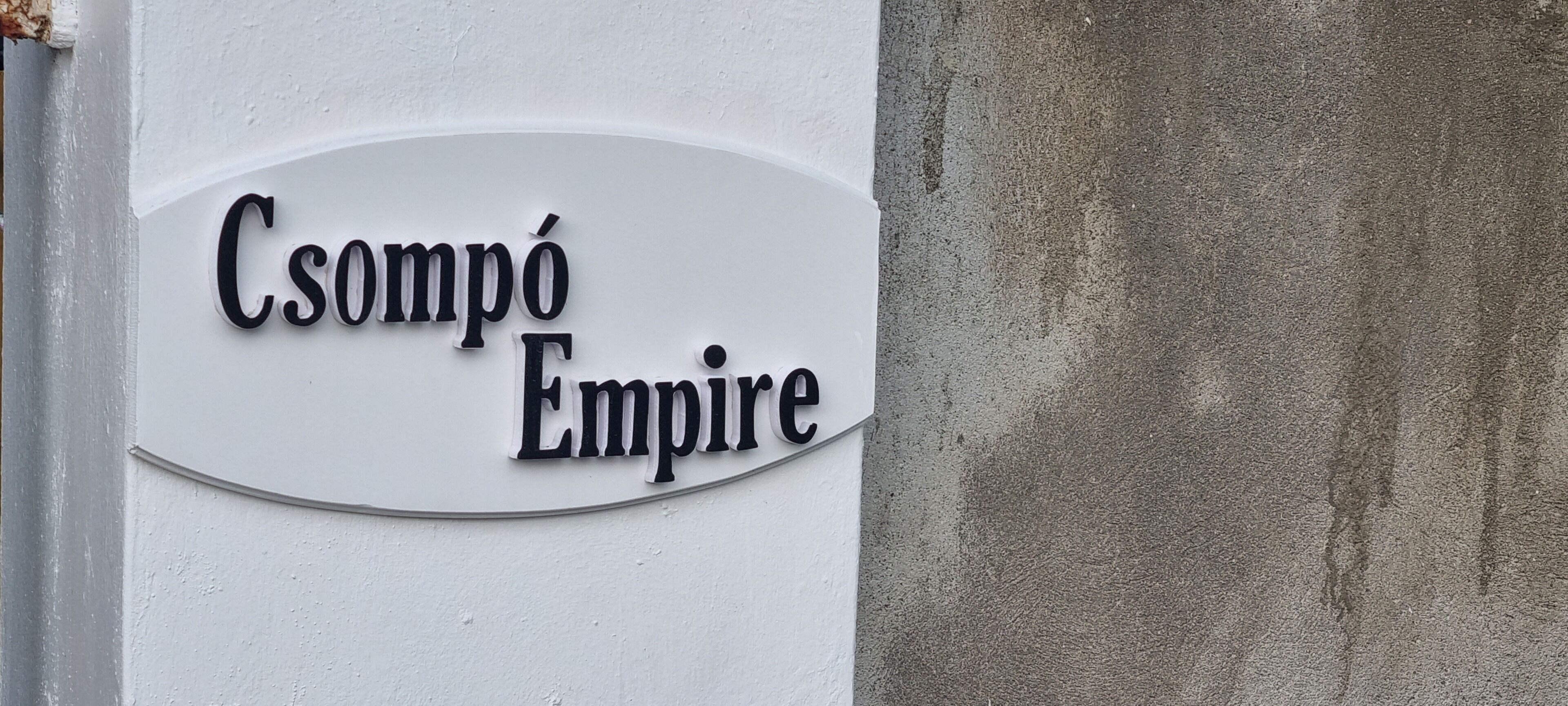 Et skilt med teksten "Csomópé Empire" på en hvid væg.