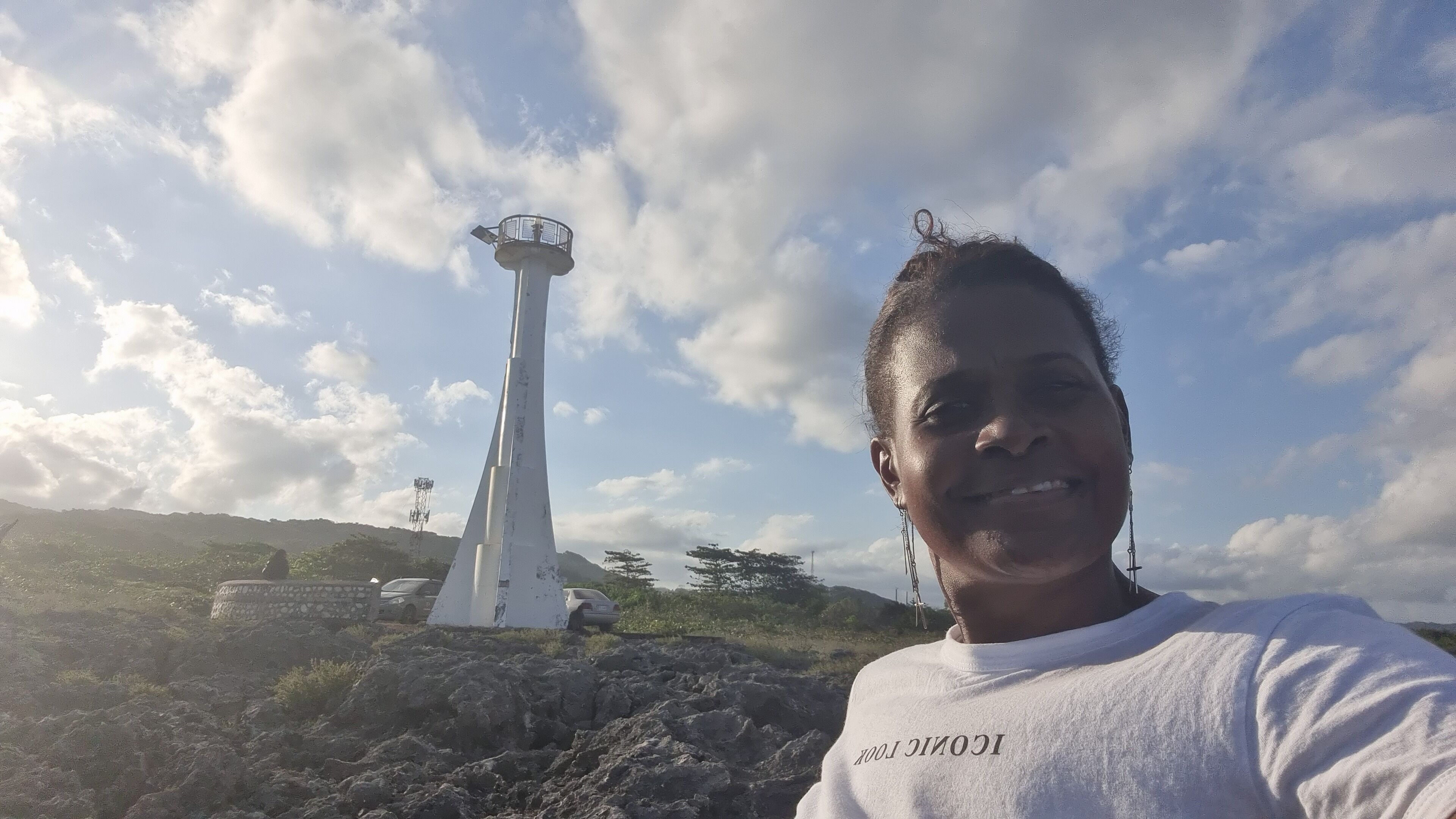 A white lighthouse with a circular platform and a spire, situated on rocky terrain with sparse vegetation.