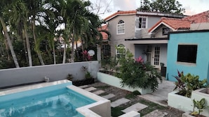 Una piscina con solárium de baldosas, rodeada de plantas en macetas y un pequeño jardín.