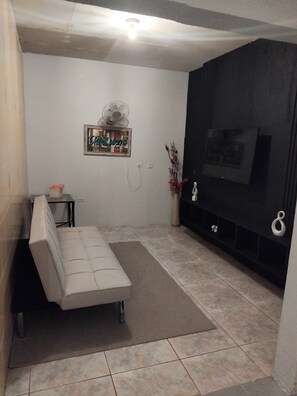 A living room with a sofa, a small table, a fan, a decorative mirror, and a TV stand. - Leisure Duplex At Csompo Silver Manor (Tower Isle)