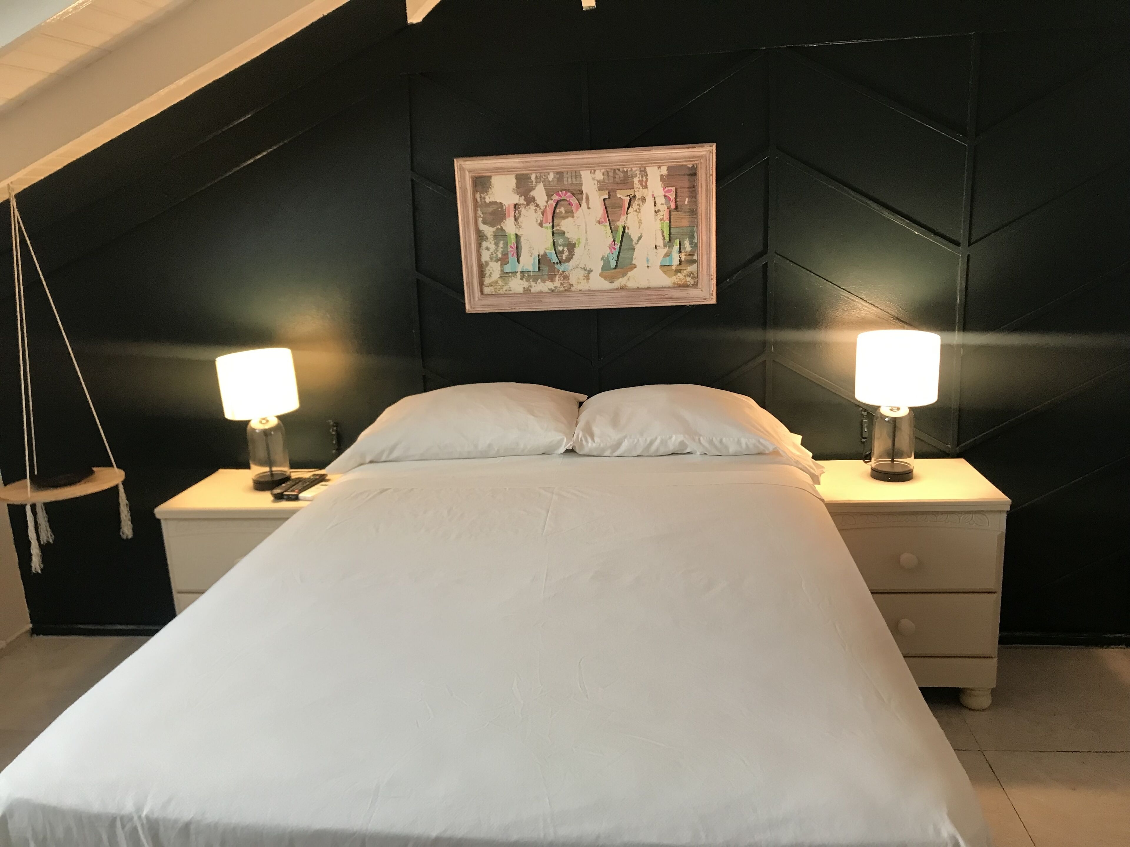 Une chambre à coucher avec un grand lit, deux tables de chevet avec des lampes, un fauteuil suspendu et un tableau accroché au mur.