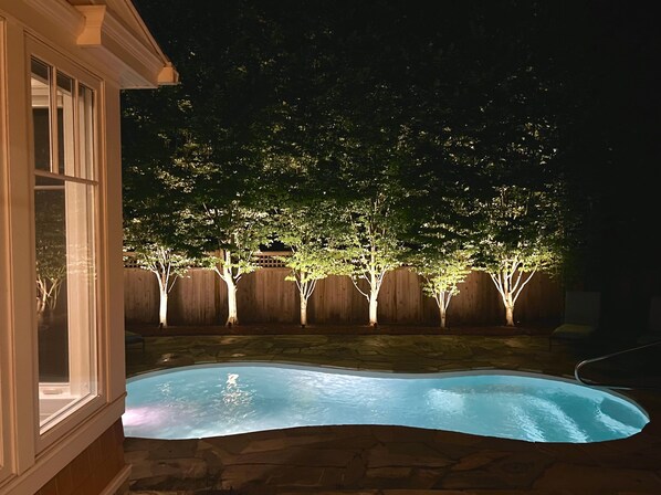 A backyard with a swimming pool, wooden fence, and trees.