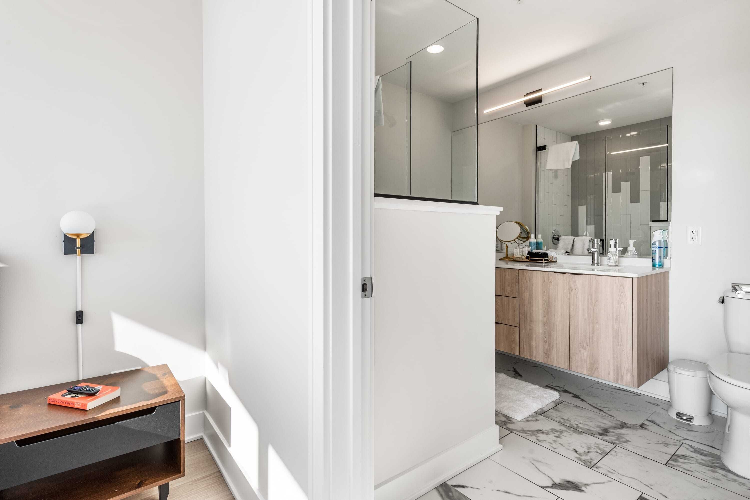 A modern bathroom with a large mirror, a wooden vanity, and a marble floor.