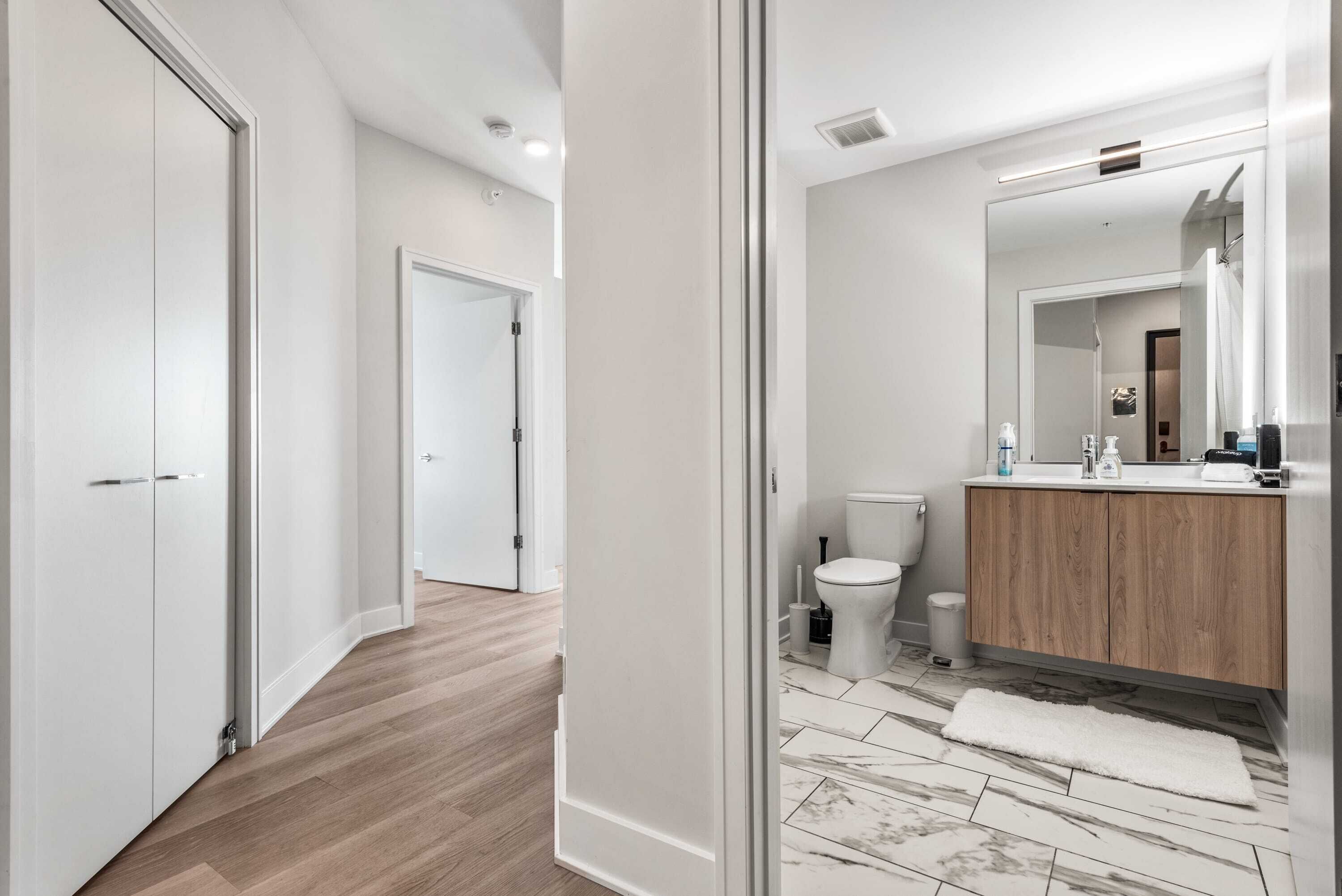 A modern bathroom with a wooden vanity, a large mirror, and a marble-tiled floor.