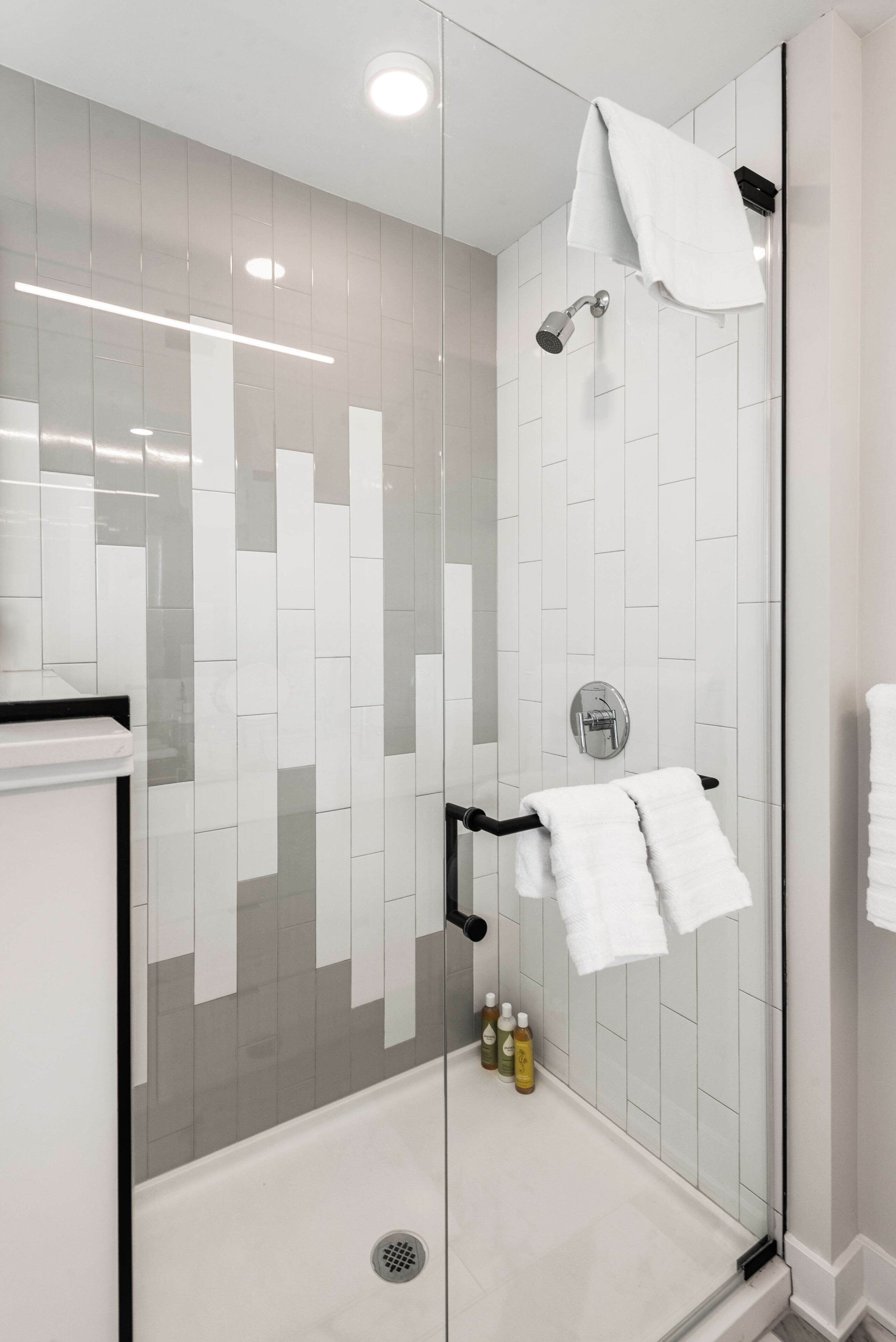 Eine moderne Dusche mit Glastür, weißen Fliesen und Duschbrause.