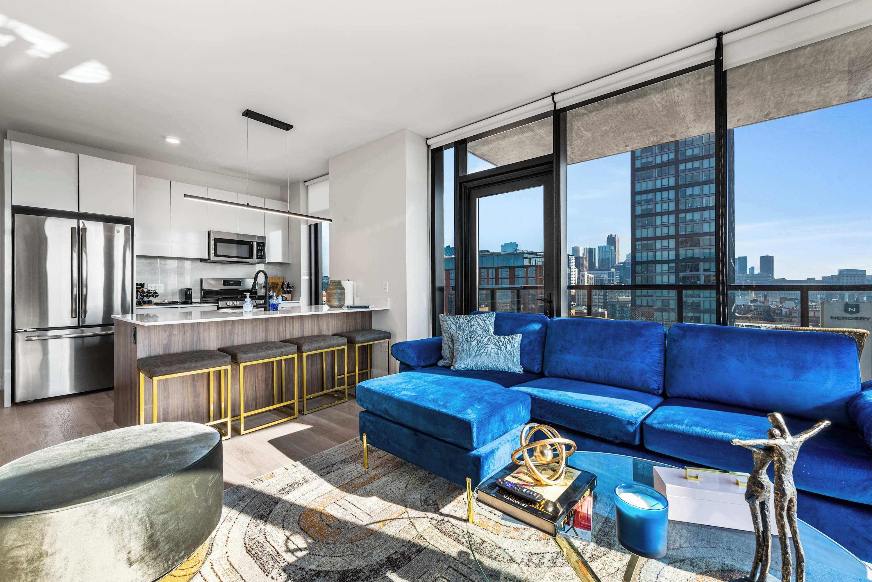 A modern apartment with a kitchen, a blue sofa, and a city view.