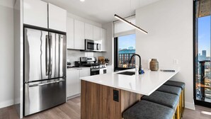 Una cocina moderna con electrodomésticos de acero inoxidable, una isla de madera y vistas a la ciudad a través de amplios ventanales.