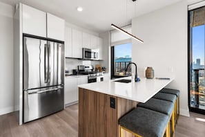 A modern kitchen with stainless steel appliances, a wooden island, and a city view through large windows.