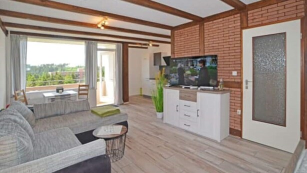 Ein Wohnzimmer mit einer Couch, einem Couchtisch, einem Fernseher auf einem Schrank und einer Glastür zum Balkon.