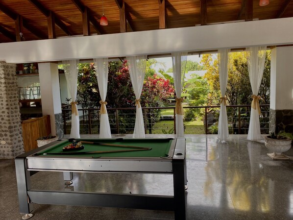 A pool table in a room with large windows, a wooden ceiling, and a view of a garden. - Stunning Volcano View • Private Pool • Near Hot Springs • Pet Friendly (Mogote de Bagaces)