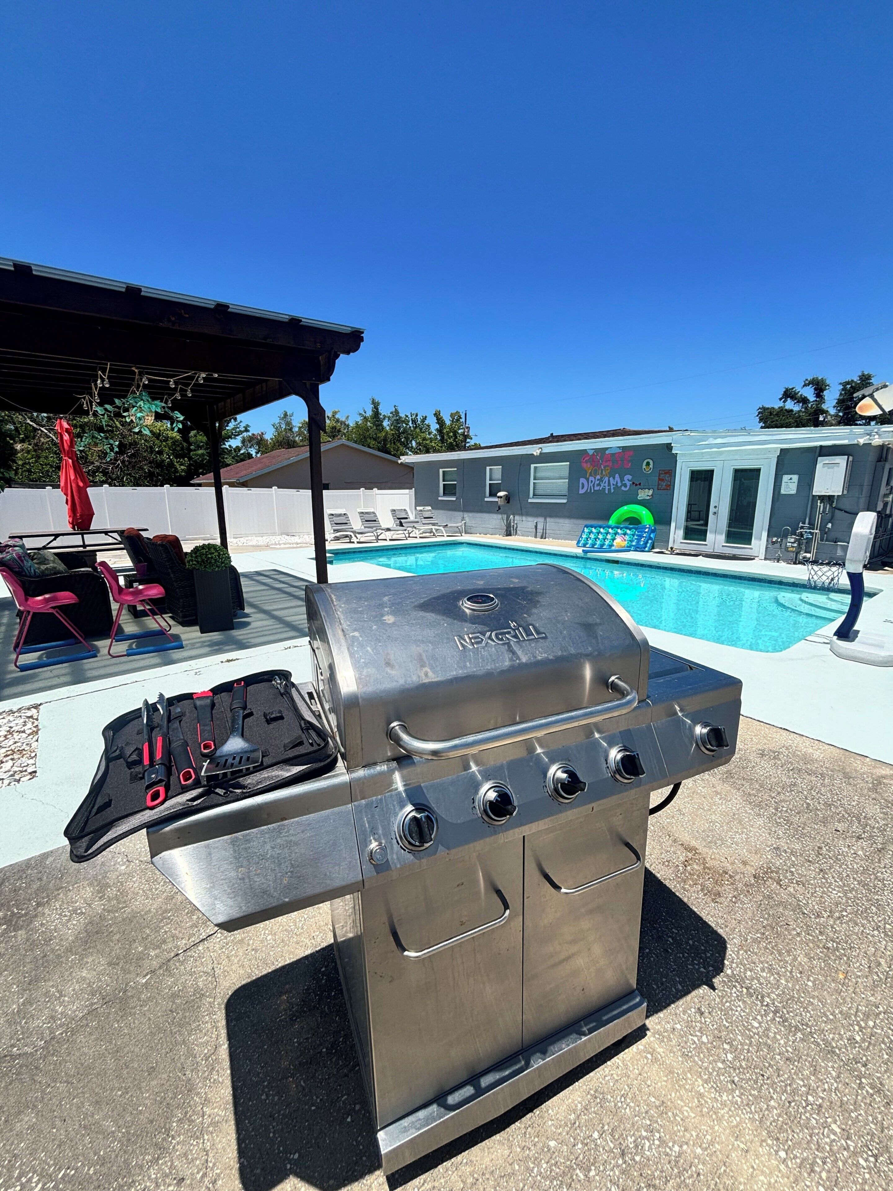 A backyard with a pool, a grill, and lounge chairs.
