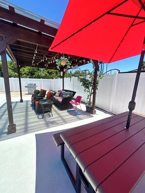 A covered patio with a red umbrella, outdoor furniture, and a grill.