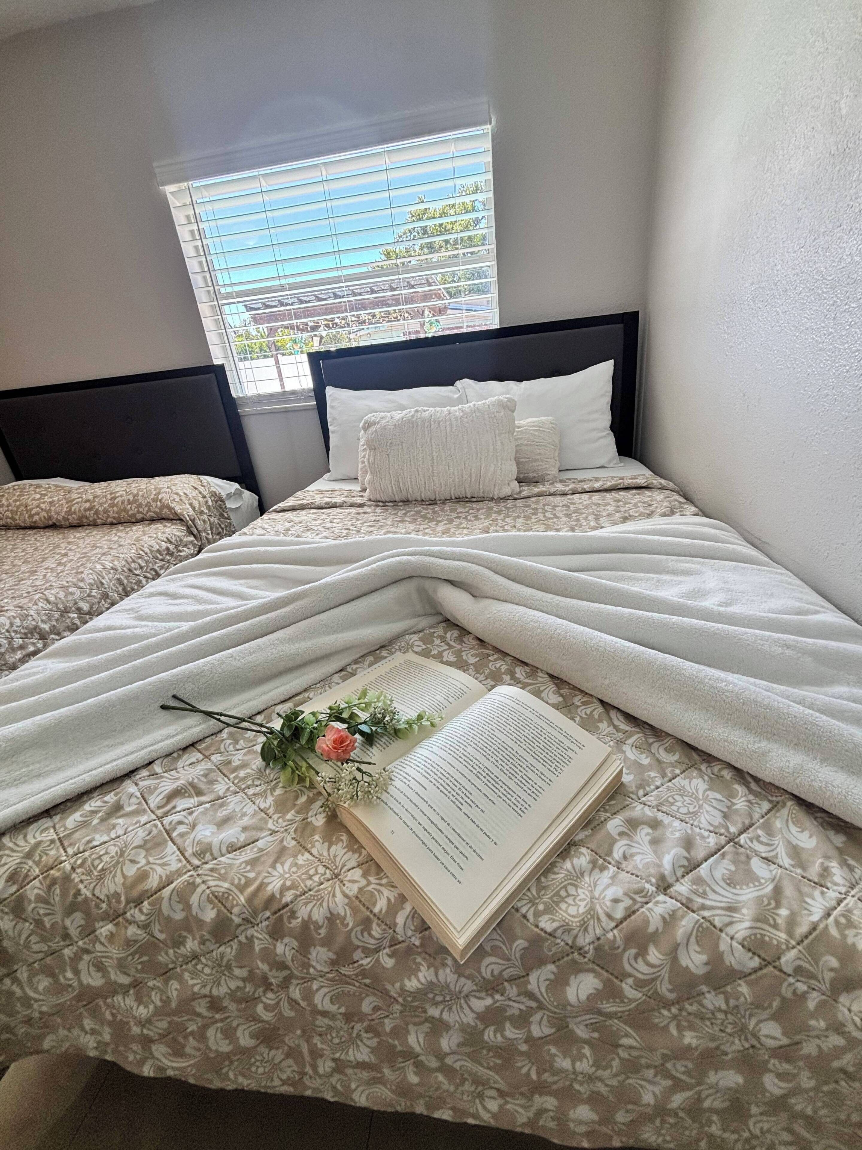 Une chambre à coucher avec un lit, une fenêtre avec des stores et un livre orné de motifs floraux.