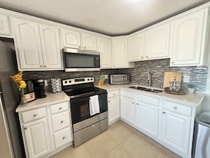 A modern kitchen with white cabinetry, a stainless steel stove, a microwave, and a toaster.