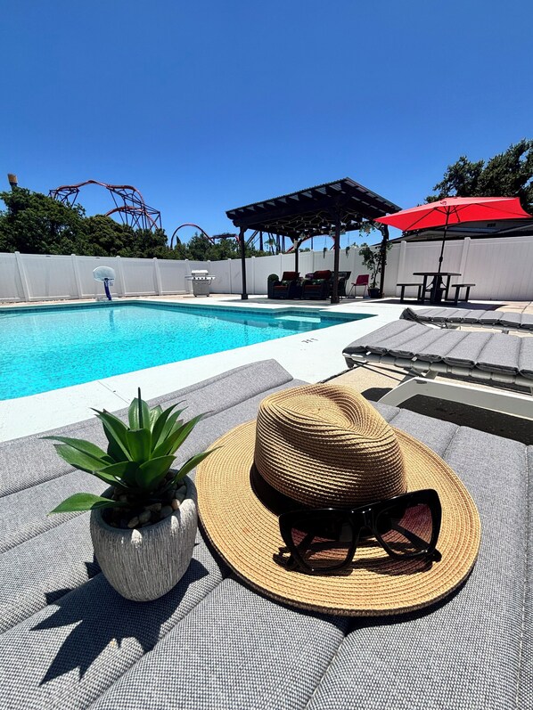 A poolside area with a lounge chair, a sun hat, and a pair of sunglasses.
