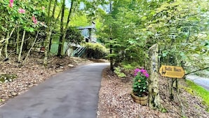 A pathway leading to a rustic building labeled "Belle Haus" surrounded by lush greenery and trees. - Storybook Chalet/Watch Movies Under the Stars/NEW Hot Tub/Hiking/Biking/Concerts (Beech Mountain)
