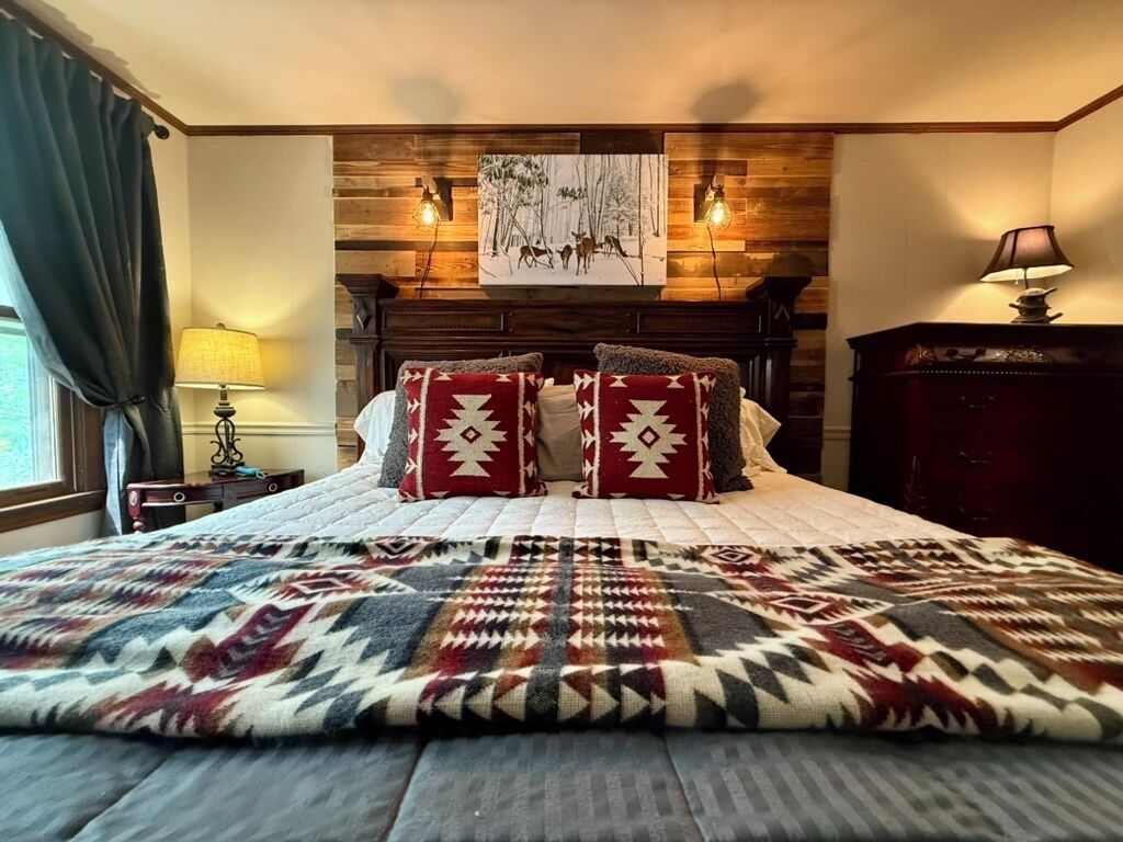 A bedroom with a bed, a wooden headboard, a wall-mounted painting, and a nightstand with a lamp.