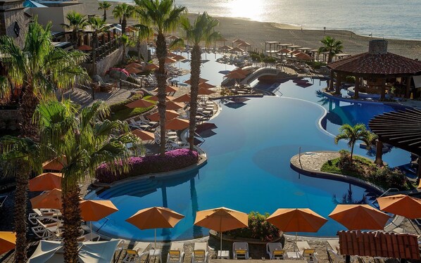 Relax by the infinity pool surrounded by palm trees and lounge chairs, offering panoramic views of the beach and ocean.