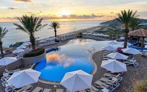 Relax by the ocean-view pool surrounded by lounge chairs and umbrellas under the shade of palm trees.