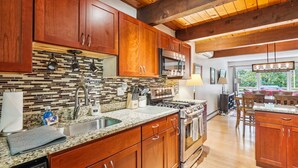 Cocina moderna con armarios de madera, encimera de granito, electrodomésticos de acero inoxidable y una lámpara colgante.