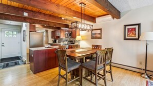Una cocina con vigas de madera, una zona de comedor con una mesa y sillas, y un refrigerador.