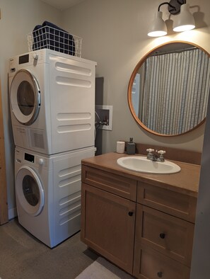 A laundry area with stacked washing machines and a sink with a mirror above it.