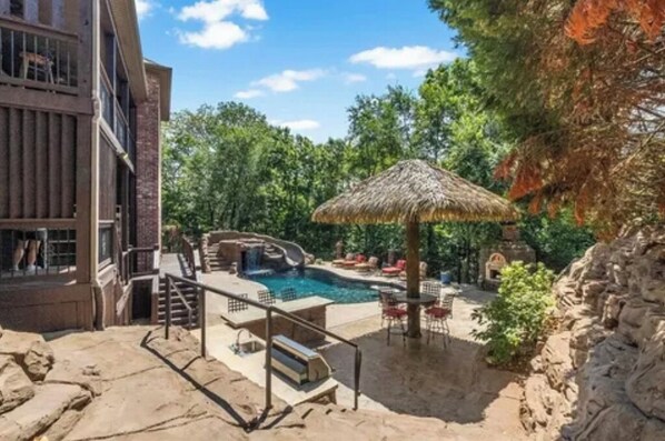 Relax by the pool surrounded by lush greenery and a shaded patio.