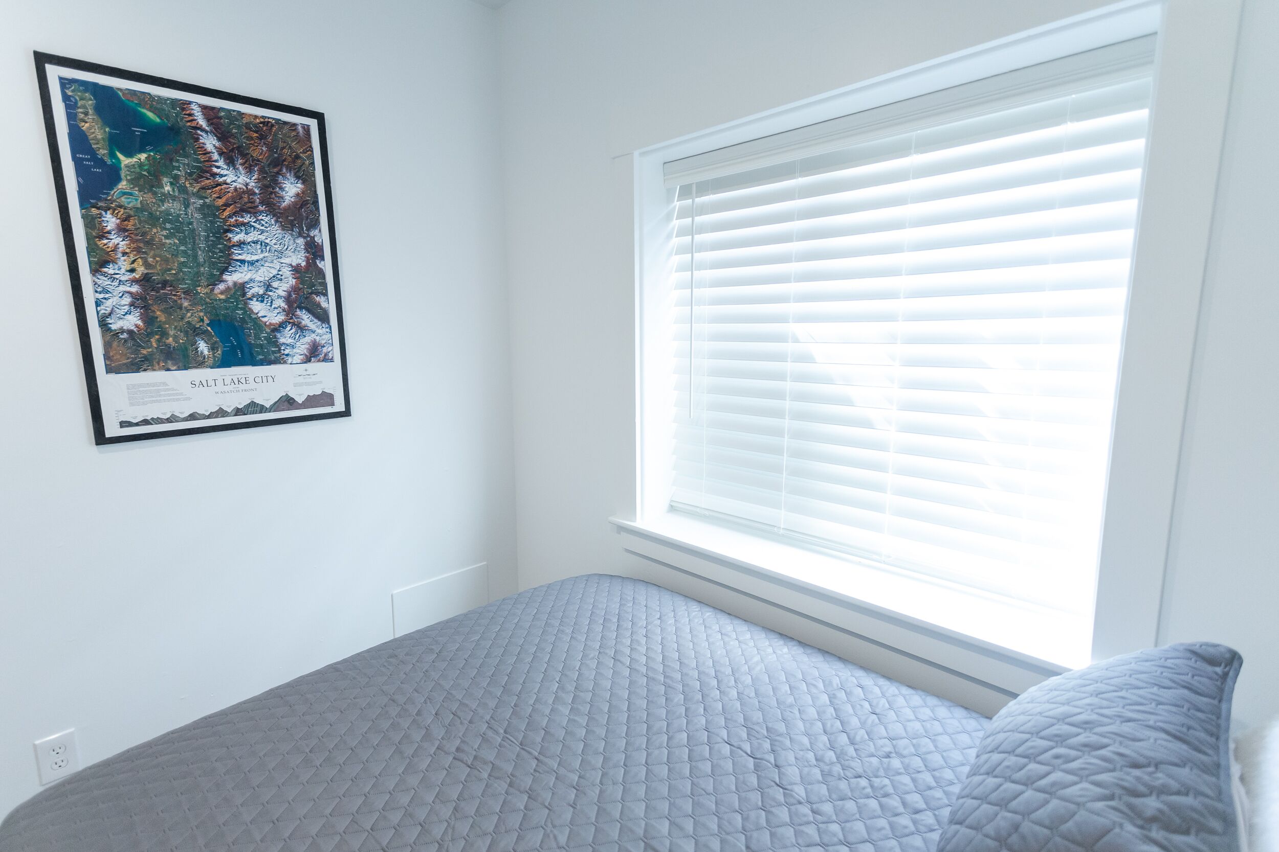 Quarto com cama, janela com persianas e um mapa emoldurado na parede.