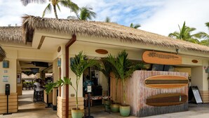 Un restaurante frente al mar con techo de paja, palmeras y una exhibición de tablas de surf.