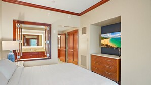 Habitación de hotel con una cama grande, una tocador con espejo, un aparador y un televisor montado en la pared mostrando una escena de playa.
