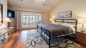 A bedroom with a bed, bedside tables, a TV, and a view through a sliding glass door. - Soothe Your Soul Lakeside on Beautiful Lake Balboa (Hot Springs Village)