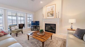 A living room with a fireplace, a television, and a large window overlooking a snowy landscape. - Soothe Your Soul Lakeside on Beautiful Lake Balboa (Hot Springs Village)